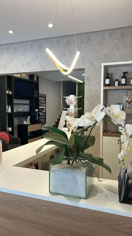 Orquídea branca sobre o balcão claro da recepção, com prateleiras de produtos ao fundo